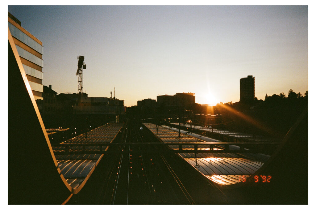Analoges Filmfoto vom Sonnenuntergang über den Bahnhof Bern: Die sogenannte Welle erstrahlt goldig dank den letzten Sonnenstrahlen.